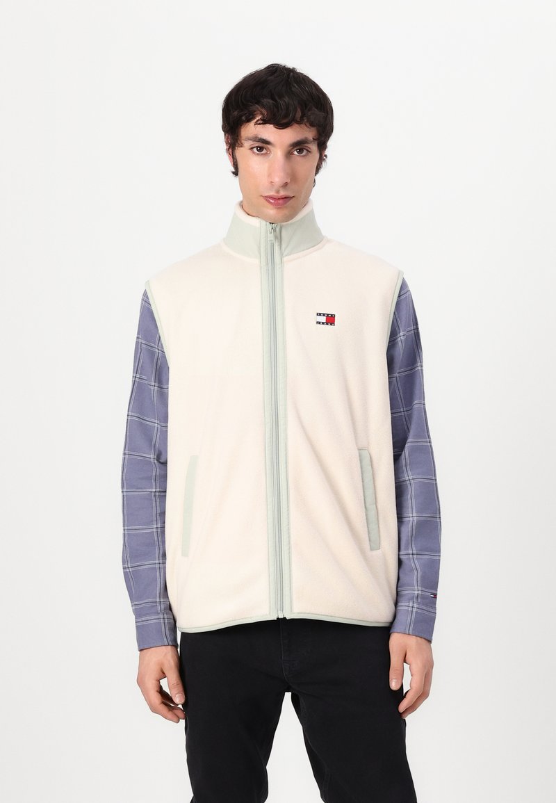 Lys beige fleecevest med høy krage og frontglidelås. Har to sidelommer, grå detaljer og en liten logo på brystet.