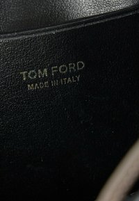 Gros plan d'une surface en cuir noir avec un texte doré en relief indiquant "TOM FORD MADE IN ITALY".