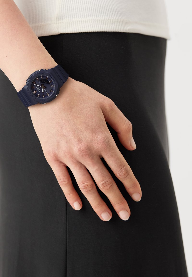 Orologio in silicone blu navy con quadrante rotondo, lunetta testurizzata e indice delle ore in argento. Posizionato su una mano che riposa su un indumento nero.