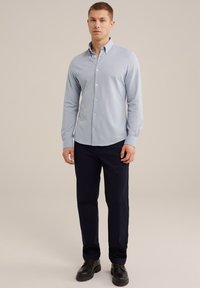 Camisa de botones de manga larga azul claro, con un corte ajustado, combinada con pantalones oscuros de color marino y zapatos negros. Tela suave con cuello.