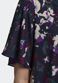 Detail na zvonových rukávech šatů s květinovým vzorem v purpurové, zelené a krémové barvě na tmavě námořnickém pozadí; hladká textura látky.