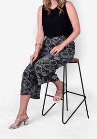 Top sin mangas negro combinado con pantalones de pierna ancha de talle alto y estampados con círculos blancos. La modelo lleva sandalias beige con tiras.