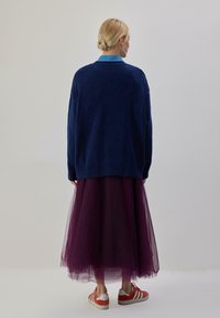 Maglione oversize blu marina, indossato sopra una gonna di tulle viola, abbinato a scarpe bianche con strisce rosse. Tessuto liscio, vestibilità rilassata.