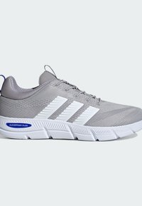 Sivé športové topánky s textúrovanou sieťovinou, bielym dizajnom s tromi pruhmi a hrubou bielou gumovou podrážkou; obsahujú Cloudfoam Flex tlmenie.