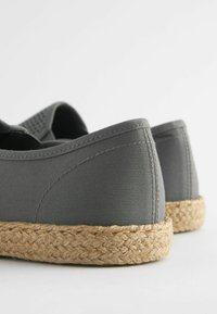 Harmaat espadrille-kengät, joissa on kangasosa ja kudottu juuteesta valmistettu pohja, varustettuna pyöristetyillä reunoilla ja ompeluvaloilla saumoissa.
