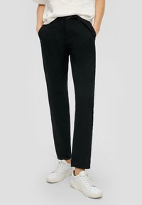 Zwarte rechte pantalon met een gladde textuur, voorzien van voorkeurszakken en een subtiele taillebanddetail. Gepaard met witte sneakers.