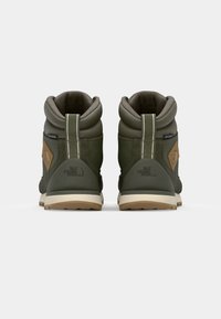 Bottes vert olive avec une tige texturée, un col rembourré et une semelle en caoutchouc beige clair. Présente un logo de marque au niveau du talon et sur le côté.
