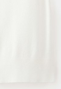 Tissu de pull tricoté blanc avec détail de bord-côtes en bas, montrant la texture et le motif de tricot en gros plan.