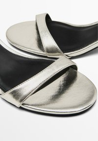 Metaliczne srebrne sandały z szerokim paskiem o gładkim wykończeniu, miękką czarną wkładką i eleganckim, minimalistycznym designem.