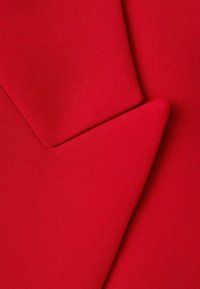 Close-up of red fabric lapel and notch detailing on a tailored garment, highlighting smooth texture and sharp edges.