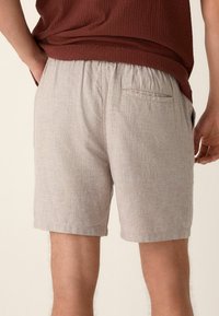 Vista trasera de una persona que lleva pantalones cortos de color beige claro con una cinturilla elástica y un solo bolsillo trasero en el lado derecho.