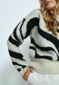 Maglione lavorato a maglia con motivo a strisce zebra in crema e nero. Presenta un collo e polsini a costine, una vestibilità comoda e una texture morbida.