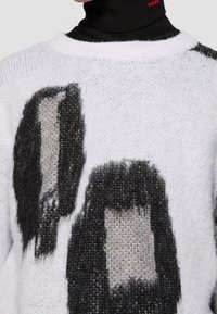 Strickpullover in Weiß mit großen schwarz- und graufarbenen abstrakten Formen. Verfügt über eine weiche Textur und einen runden Ausschnitt. Rotierende Farbtöne verleihen Tiefe.
