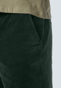 Donkergroene corduroy broek met een gestructureerde afwerking en zijzakken, gecombineerd met een licht olijfgroen shirt met korte mouwen.