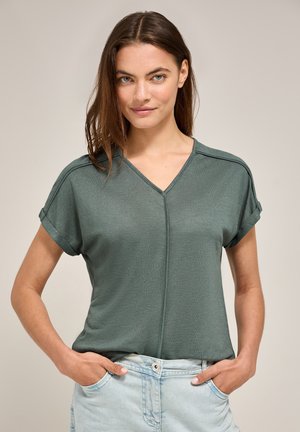 Grøn bluse med korte ærmer og V-hals, med en tekstureret finish og opsmøgede manchetter. Sammen med lyseblå jeans.