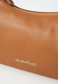 Smeđi kožni ručno izrađeni torba s zlatnim zatvaračem i utisnutim logotipom "VALENTINO" na prednjoj strani. Glatka površina s suptilnim sjajem.