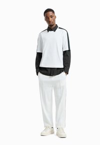Wit en zwart gelaagd shirt met lange mouwen en knopenkraag, gecombineerd met witte broek met zijstrepen en witte sneakers.