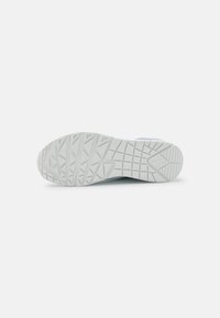 Schuhsohle, Gummi-Material, strukturierte Oberfläche mit einem dreieckigen Muster, überwiegend weiß mit glatter Oberfläche, zulaufender Zehenbereich.