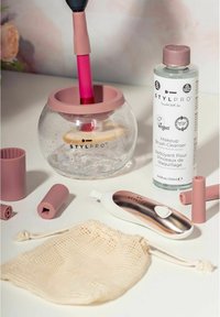 Stylpro sminkborstrenare med klart glas och rosa silikonaccenter, tillsammans med en flaska borstrenare och tillbehör.