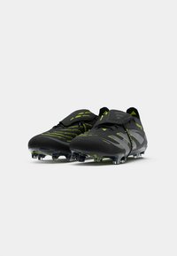 Black football boots with green accents, textured upper, round toe, and multiple studs on the sole for traction. Features Velcro straps.
