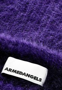 Lila flauschiger Stoff mit einem weißen ARMEDANGELS-Label, das an die Kante genäht ist.