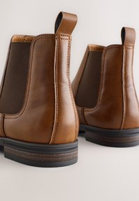 Braune Chelsea-Stiefel aus Leder mit elastischen Seitenteilen, abgerundeter Zehenpartie und rutschfesten Sohlen. Verfügen über erhöhte Nahtdetails und Zuglaschen für einfaches An- und Ausziehen.