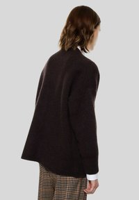 Maglione marrone oversize realizzato in morbido tessuto a maglia strutturato. Presenta un orlo posteriore arrotondato e maniche larghe, abbinato a pantaloni stampati.