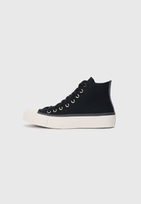 Sneakers alti in tela nera con suole in gomma bianca, dotati di occhielli in metallo e una superficie testurizzata lungo il lato.