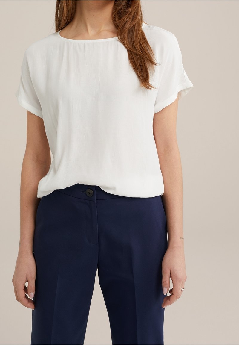 Vit kortärmad blus i lättviktigt tyg, med rund halsringning och avslappnad passform, tillsammans med marinblå skräddarsydda byxor.