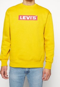Gelbes Sweatshirt aus Baumwollmischung mit einem roten Levi's Logo-Graphic auf der Vorderseite, Rippbündchen und Rundhalsausschnitt.