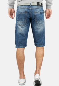 Shorts en denim bleu avec une finition décolorée, dotés de deux poches arrière et de passants de ceinture. Design à jambe droite, avec des ourlets retroussés, associés à des baskets blanches.
