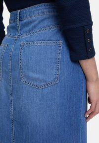 Jupe en denim bleu clair à taille haute, avec une couture de dos, deux poches arrière et des accents de couture dorée.