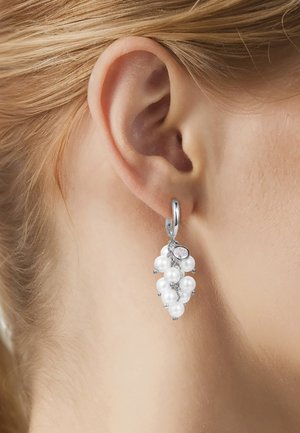 Pendiente de aro de plata con un conjunto de perlas blancas y una pequeña piedra preciosa clara, usado en la oreja de una persona de piel clara con cabello rubio.