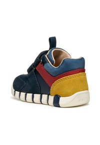 Zapatillas infantiles con materiales mixtos en azul marino, rojo y amarillo. El diseño de caña baja presenta un upper suave de ante y malla con una correa de gancho y bucle.