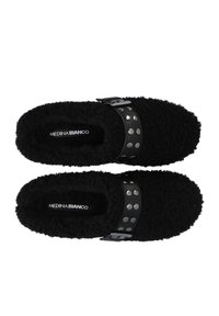 Sorte fuzzy slippers med et struktureret stof, der har et fladt design og en skinnende sort rem med sølvnitter over midtfoden.