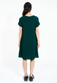 Rochie verde fără mâneci, cu o croială lejeră, având guler rotund, închidere cu fermoar la spate și slituri discrete în spate.