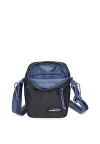 Kompaktní černá a modrá ramenní taška Eastpak s nastavitelným popruhem a otevřenou hlavní přihrádkou, která ukazuje vnitřní zipovou kapsu.