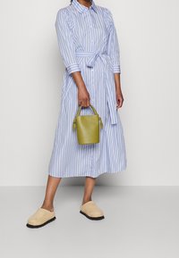 Gestreepte blauwe jurk met een tailleriem, beige instap schoenen en een groene leren tas. De jurk heeft driekwart mouwen en een ontspannen pasvorm.