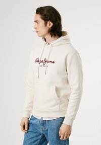 Crème hoodie met trekkoorden, voorzien van een bordeaux logo "Pepe Jeans London" op de voorkant, gecombineerd met blauwe spijkerbroeken.