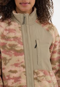 Fleecejacka med ett texturerat mönster i beige och rosa kamouflage, med dragkedja framtill och en bröstficka på en slät panel.