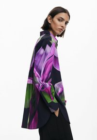 Camicia a maniche lunghe con una grande stampa floreale in viola e verde su sfondo nero; tessuto morbido e vestibilità comoda con orlo arrotondato.