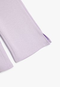 Pantalones de algodón lilas con una textura suave, piernas ligeramente acampanadas y aberturas laterales en el dobladillo. Detalles de costura visibles a lo largo de los bordes.