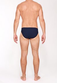 Dunkelblaue Schwimmslips mit weißen Punkten, die eine konturierte Form und einen elastischen Bund haben, von hinten betrachtet.