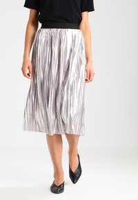 Silverfärgad plisserad midikjol med en texturerad lyster, svart elastisk midja och en flödande design, i kombination med svarta ballerinas.