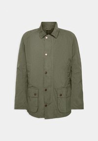 Oliwkowa kurtka z bawełny, z kołnierzem, przednimi guzikami, dwoma dużymi kieszeniami naszytymi i w kratkę podszewką.