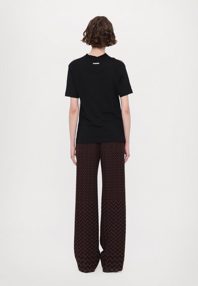 Camiseta negra de manga corta y cuello redondo, combinada con pantalones de pierna ancha que presentan un patrón de zigzag marrón.