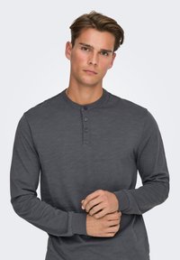 Henley-shirt met lange mouwen in donkergrijs, met een ronde hals, een drukknoopsluiting met drie knopen en geribbelde manchetten, gemaakt van een zachte, lichtgewicht stof.