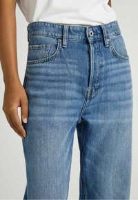 Light blue denim jeans with a straight leg design, featuring topstitching and a front pocket. Fabric displays a soft, textured finish.