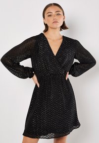 Czarna sukienka o długim rękawie z głębokim dekoltem w kształcie litery V i wzorem w zygzaki. Wykonana z przejrzystego, teksturowanego materiału, z dopasowaną talią i zwiewnym dołem.