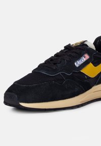 Sneaker in suede nero e rete con dettagli gialli, logo sulla linguetta e suola intermedia color crema. Presenta una punta arrotondata e un design della parte superiore testurizzato.